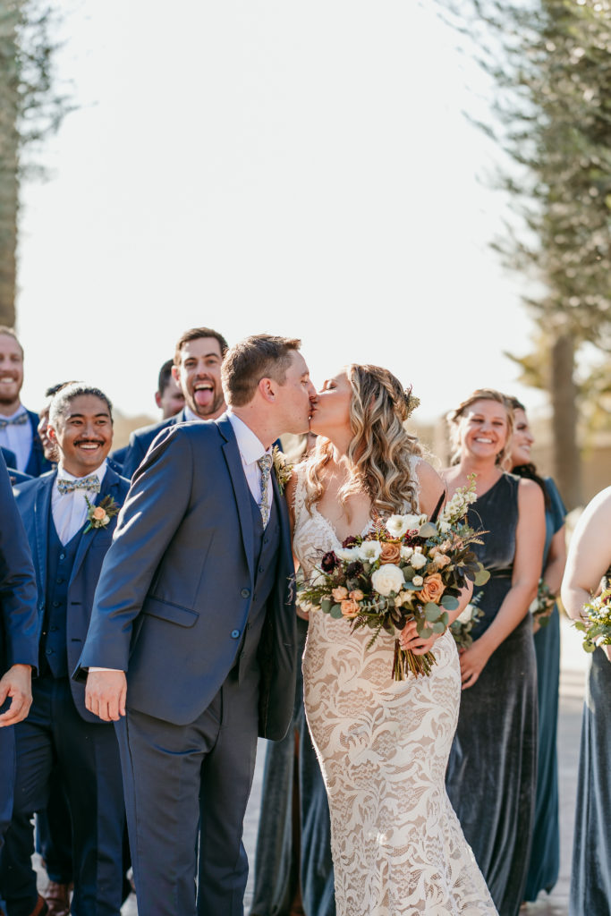 newlyweds kissing while surrounded by their bridal party