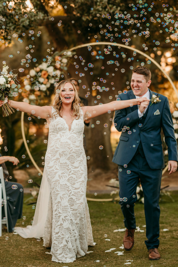 bride throwing her arms out wide in excitement as she walks through her bubble exit during her wedding ceremony