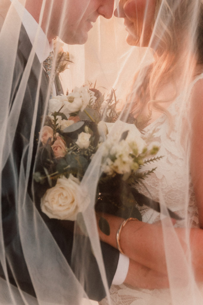 Film inspired close up of bride and groom snuggled under her veil in the evening light