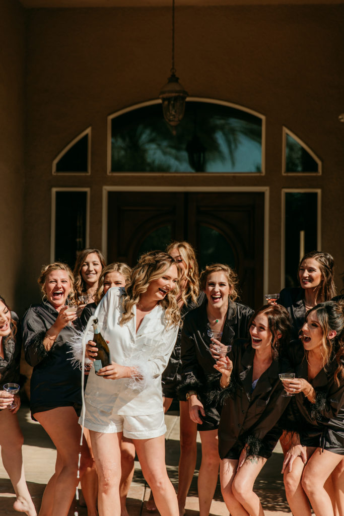 the bride and her bridesmaids popping champagne together before she ties the knot